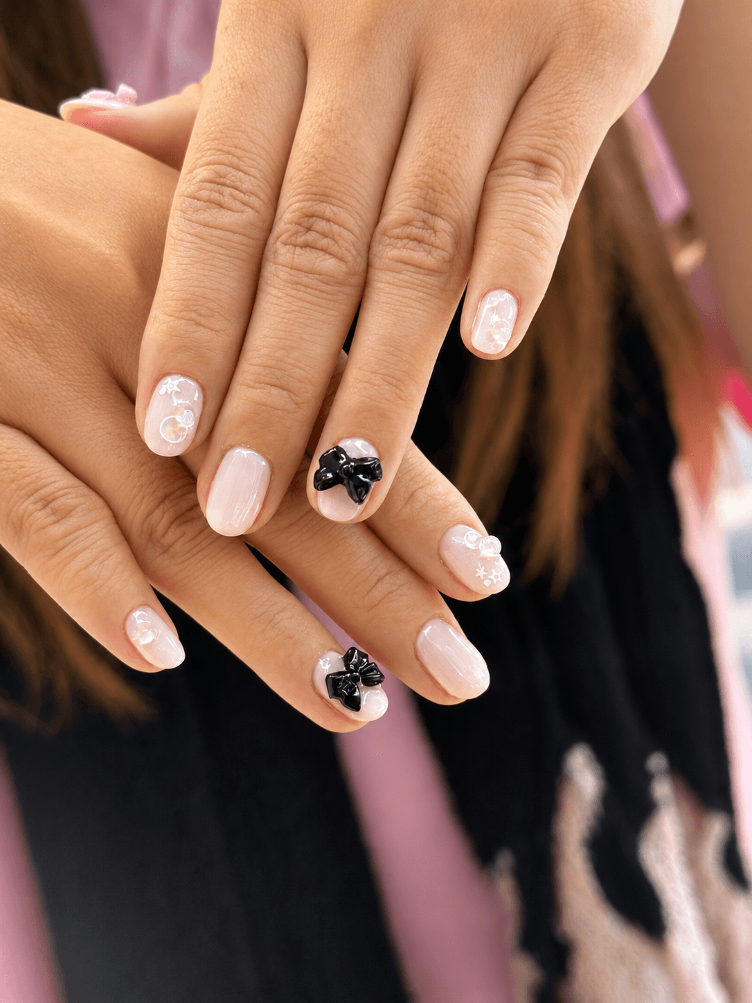 Soft pink nails with black bow accents and delicate white details